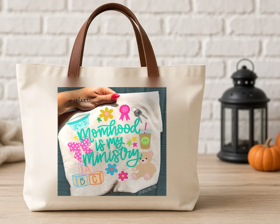 Motherhood Is My Ministry PNG design on a canvas tote bag